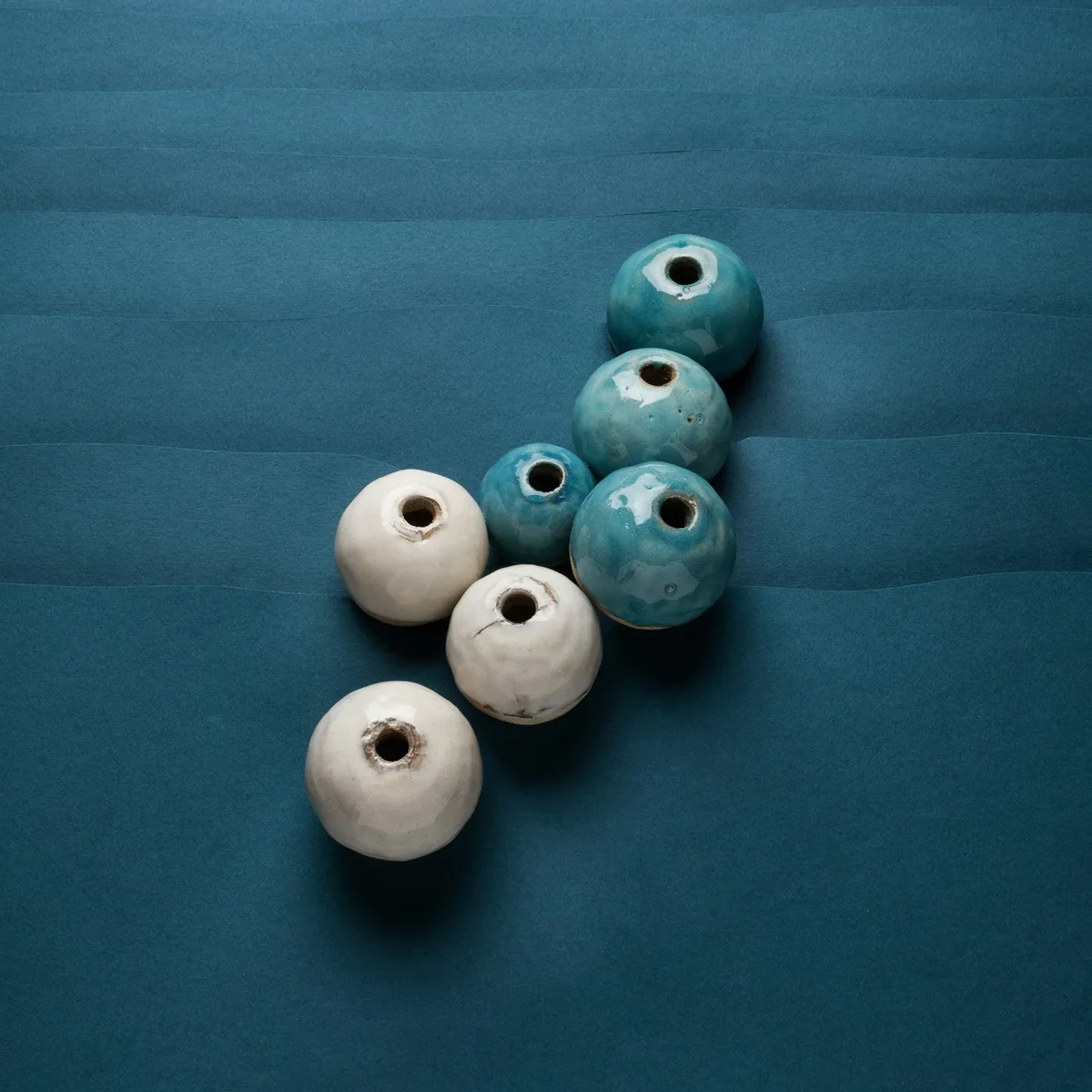 Three chipped white ceramic beads and four glossy cyan ones in a diagonal cluster, resting on layered navy paper